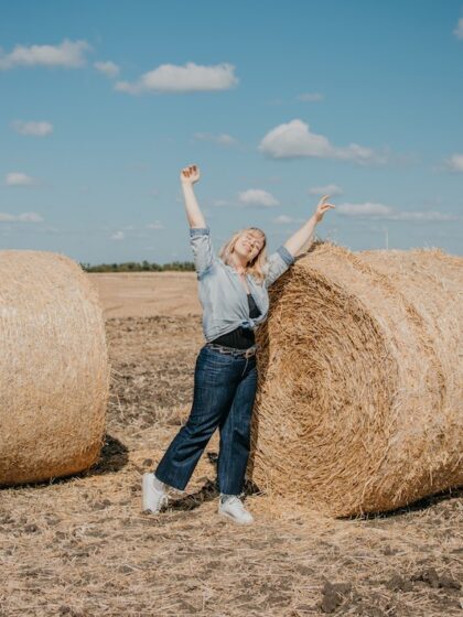 Body positive, high self esteem freedom, concept. Plus size Overweight woman celebrating rising hands to the sky and enjoys life on mowed wheat field with straw bales on sunny summer day.