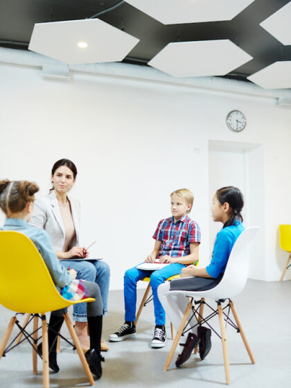 Young teacher and two classmates listening to schoolgirl during discussion of new topic