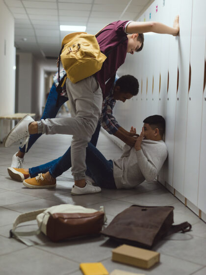 frightened asian schoolboy being bullied in school corridor