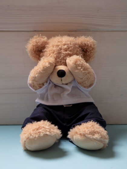 Child abuse, domestic violence concept. Teddy bear sitting alone on blue floor in an empty child room, covering eyes,